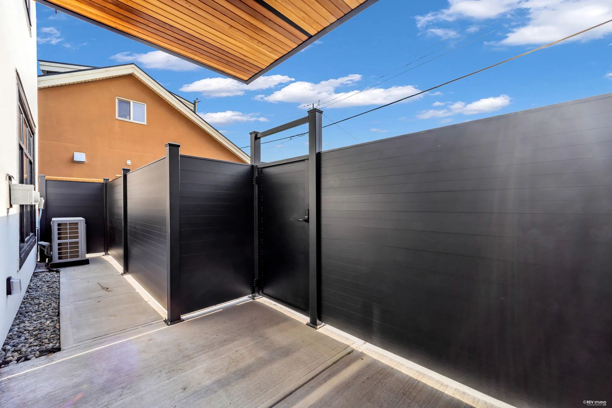 The paved patio along the side of the house, fenced